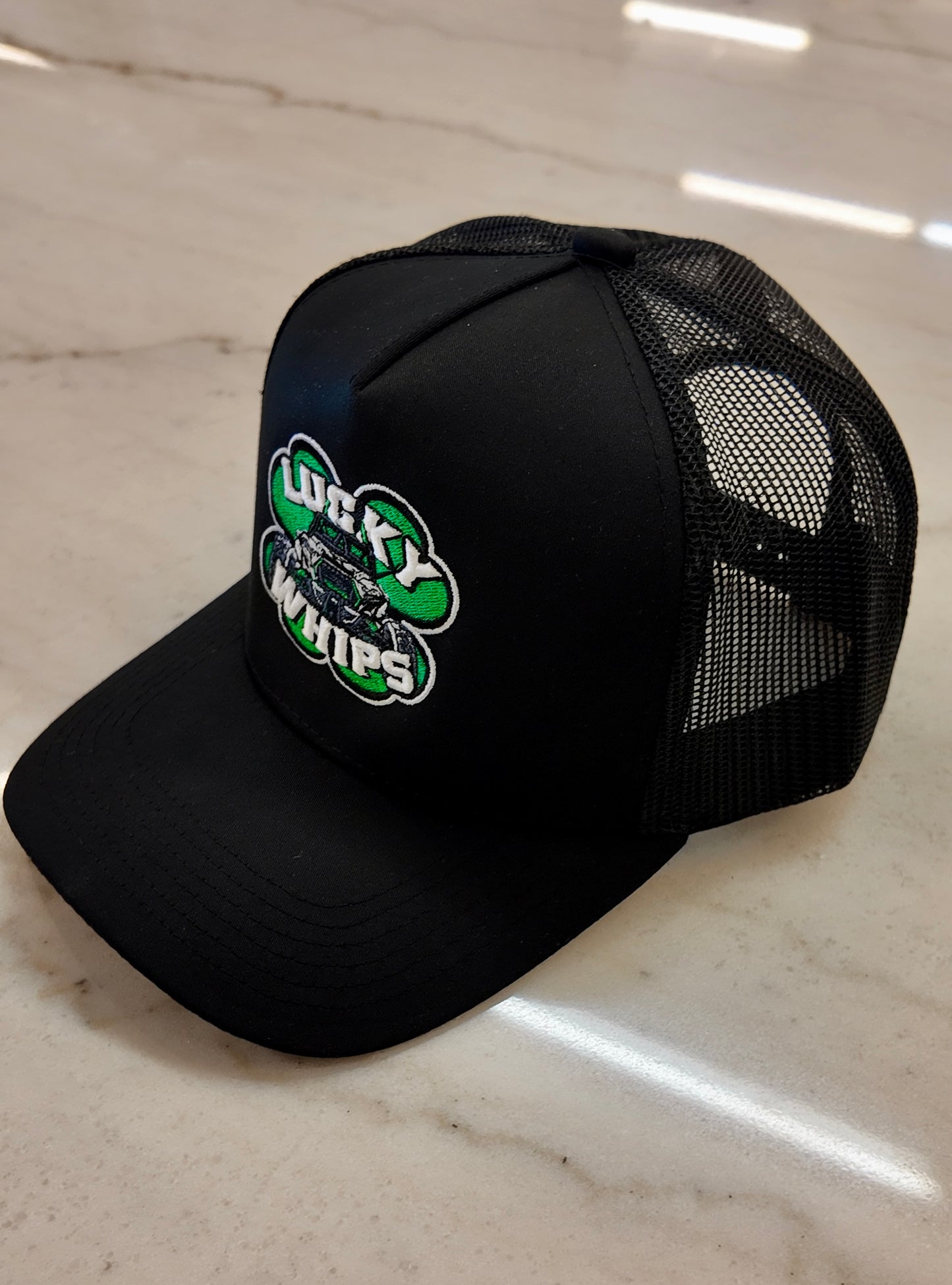 Lucky Whips Trucker Curve Bill Hat with mesh back and adjustable strap in a classic black and white design.