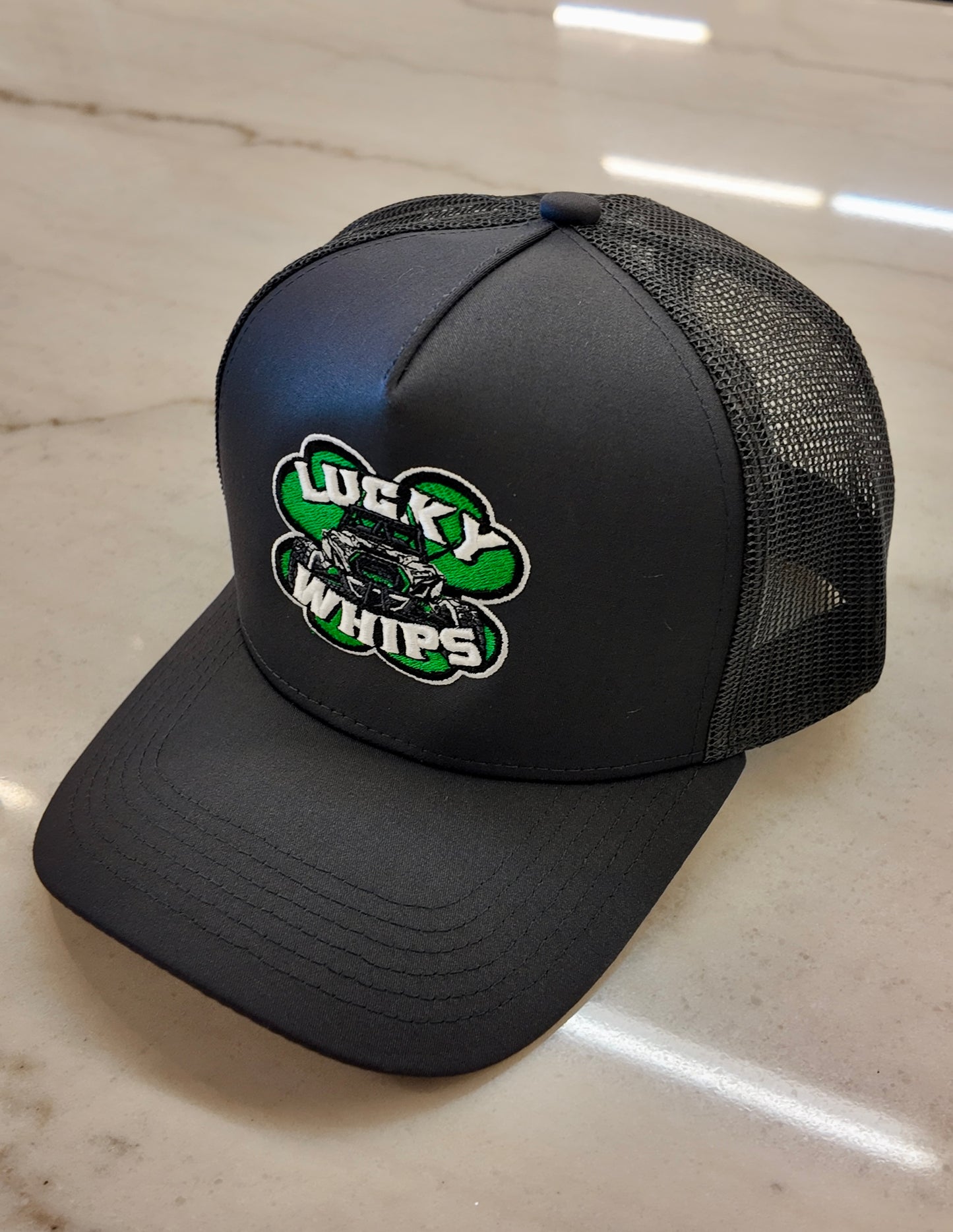 Charcoal trucker curve bill hat by Lucky Whips with mesh back and adjustable snap closure.