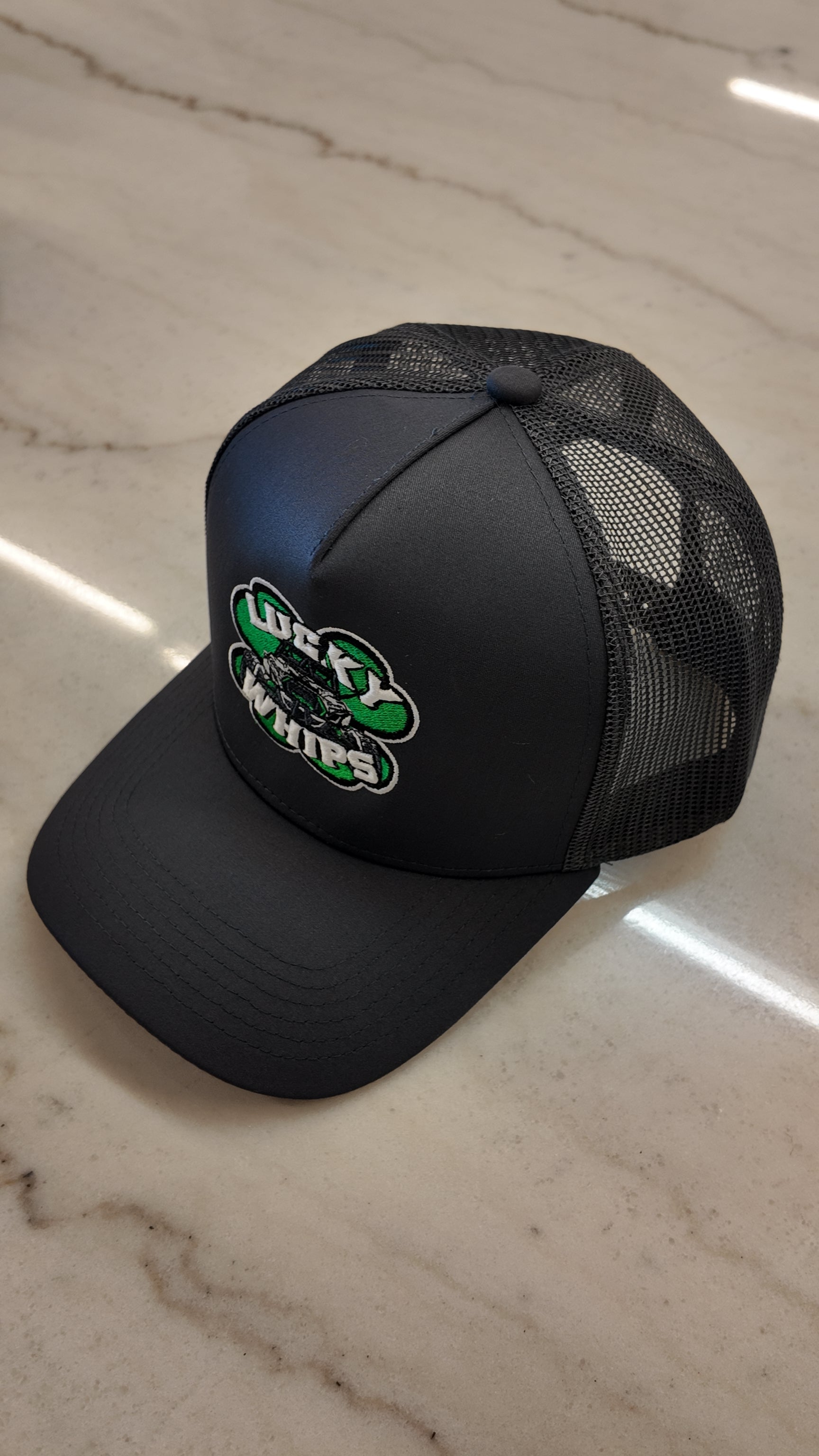 Charcoal Lucky Whips trucker hat with a curved bill and mesh back, showcasing a stylish and casual design.