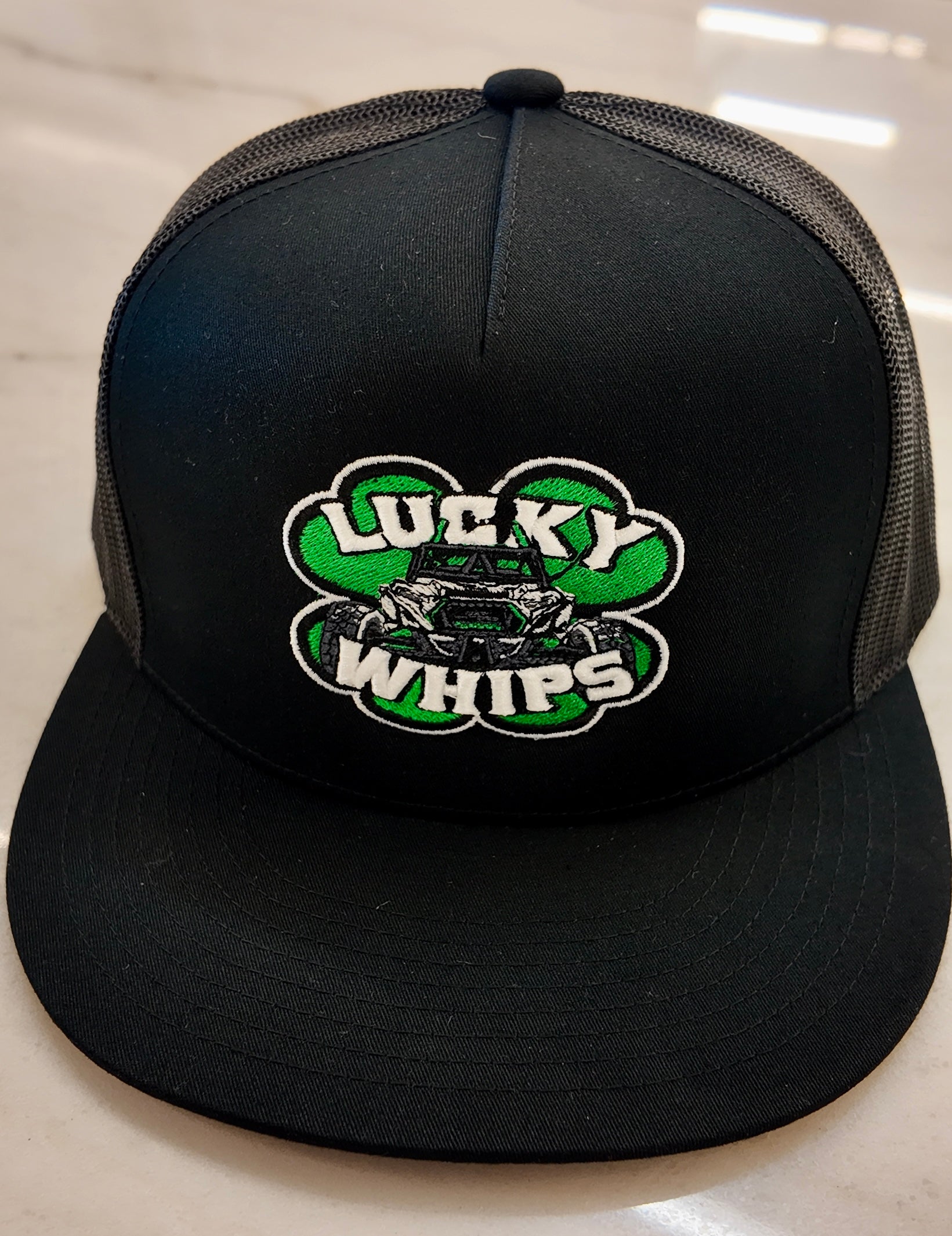 Lucky Whips trucker flat bill hat with a structured crown and mesh back in a stylish design.