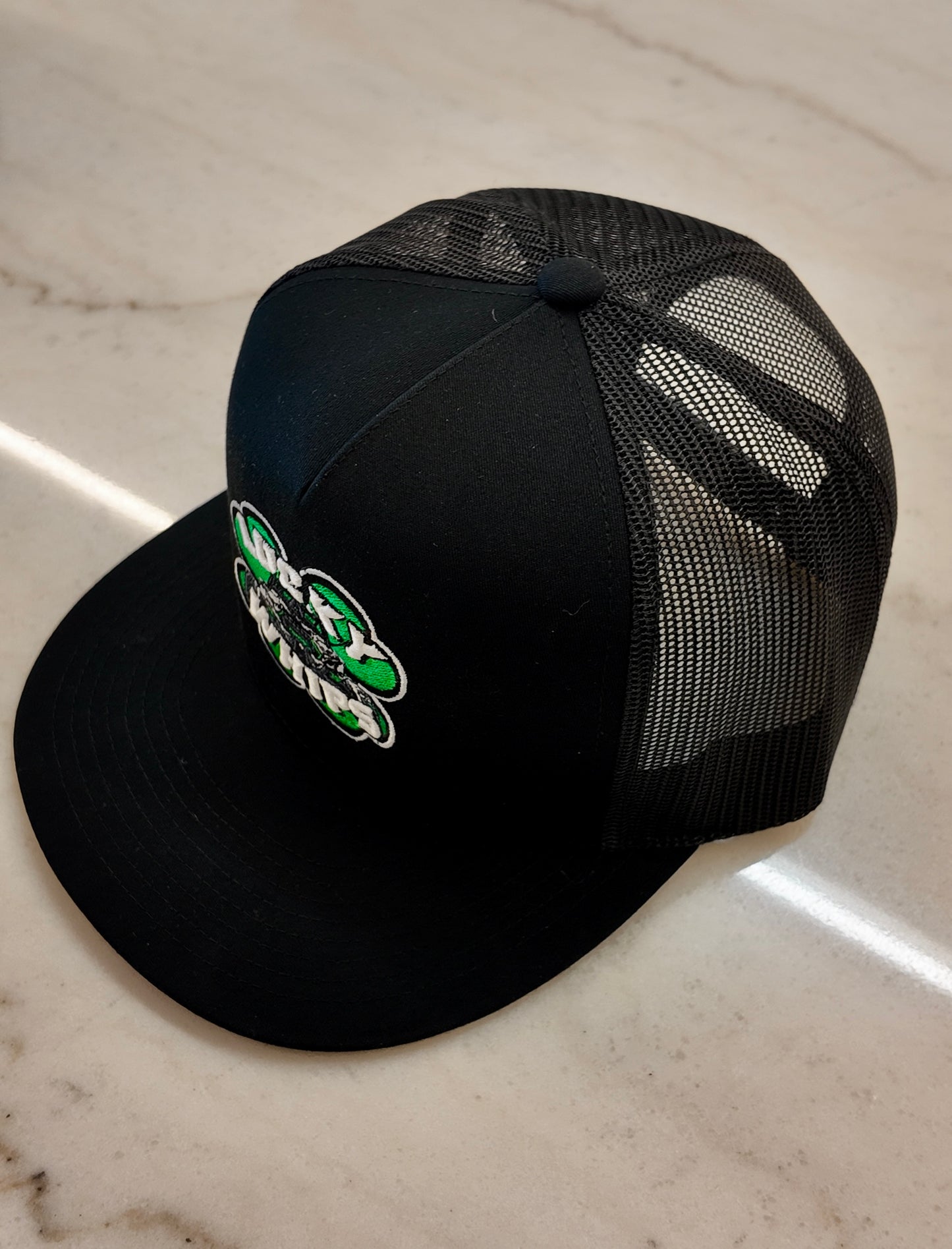 Lucky Whips trucker flat bill hat with a structured crown and mesh back, featuring a stylish black and white design.