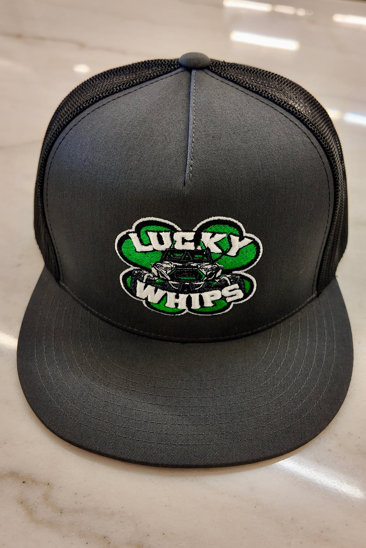 Charcoal Lucky Whips Trucker Flat Bill Hat with adjustable snapback and mesh back for a casual, stylish look.